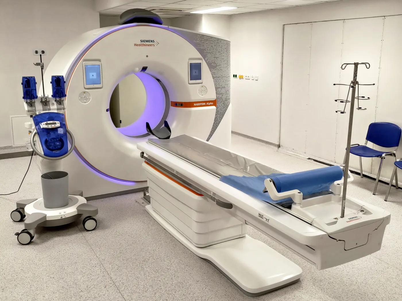 Salle de scanner avec l'anneau du tomodensitomètre et la table d'examen prête à accueillir le patient